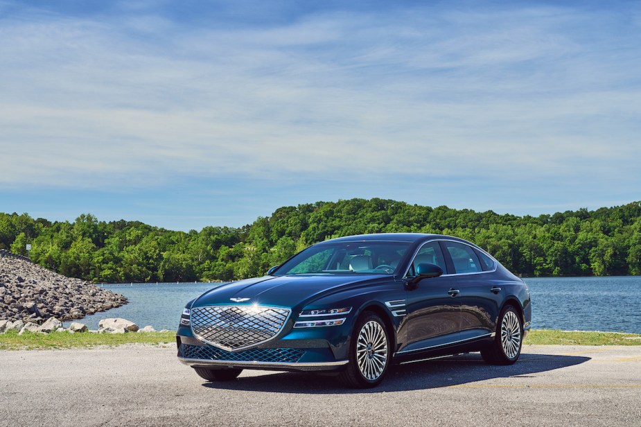 A blue 2023 Electrified Genesis GV80 parked in front of body of water. 