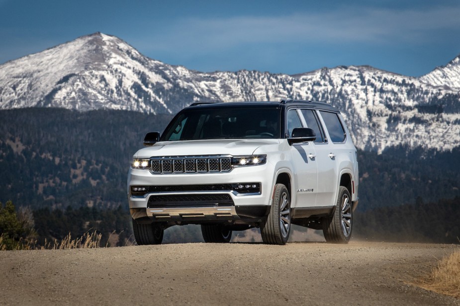 White Grand Wagoneer luxury Jeep SUV parked in front of a snow-capped mountain range.