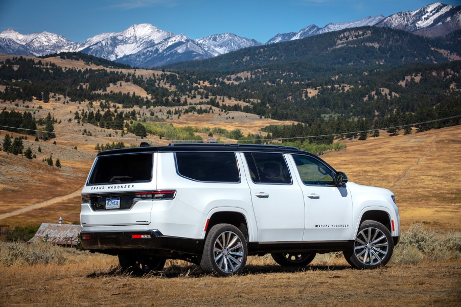 Promo photo of a white Grand Wagoneer SUV facing away from the camera, parked in front of a mountain range.