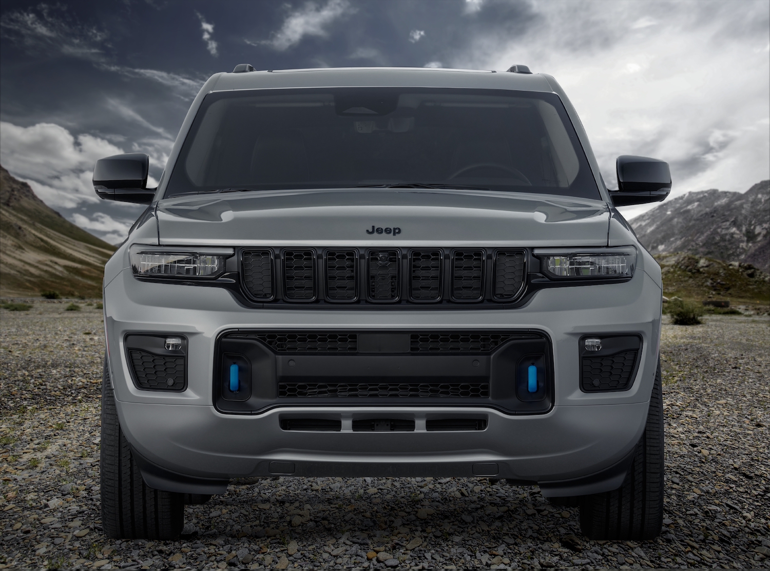 Closeup of the grille and front end of a Grand Cherokee 4xe plug-in hybrid SUV, mountains visible in the background.