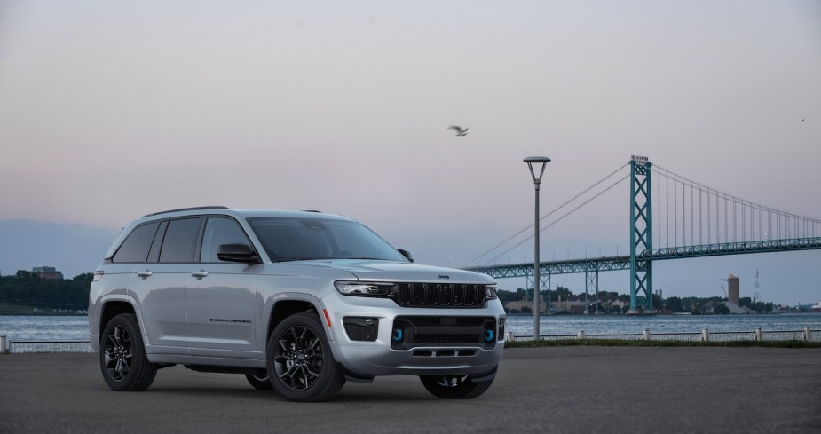 Silver Jeep Grand Cherokee plug-in hybrid SUV parked on pavement, in front of a bridge.