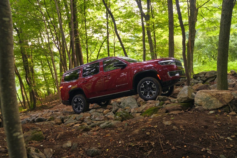 Red Wagoneer SUV climbing a rocky outcropping in the woods, trees visible in the background.