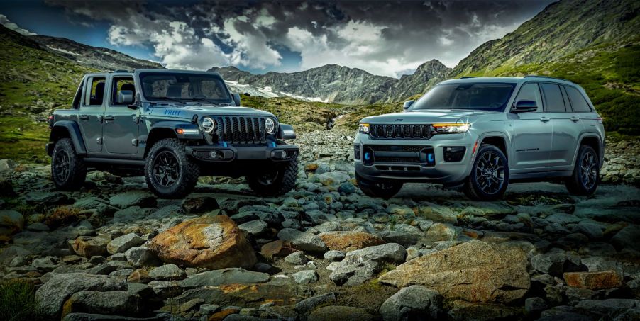 2023 Jeep Wrangler 4xe and 2023 Jeep Grand Cherokee 4xe models parked on a shore of rocks in the mountains