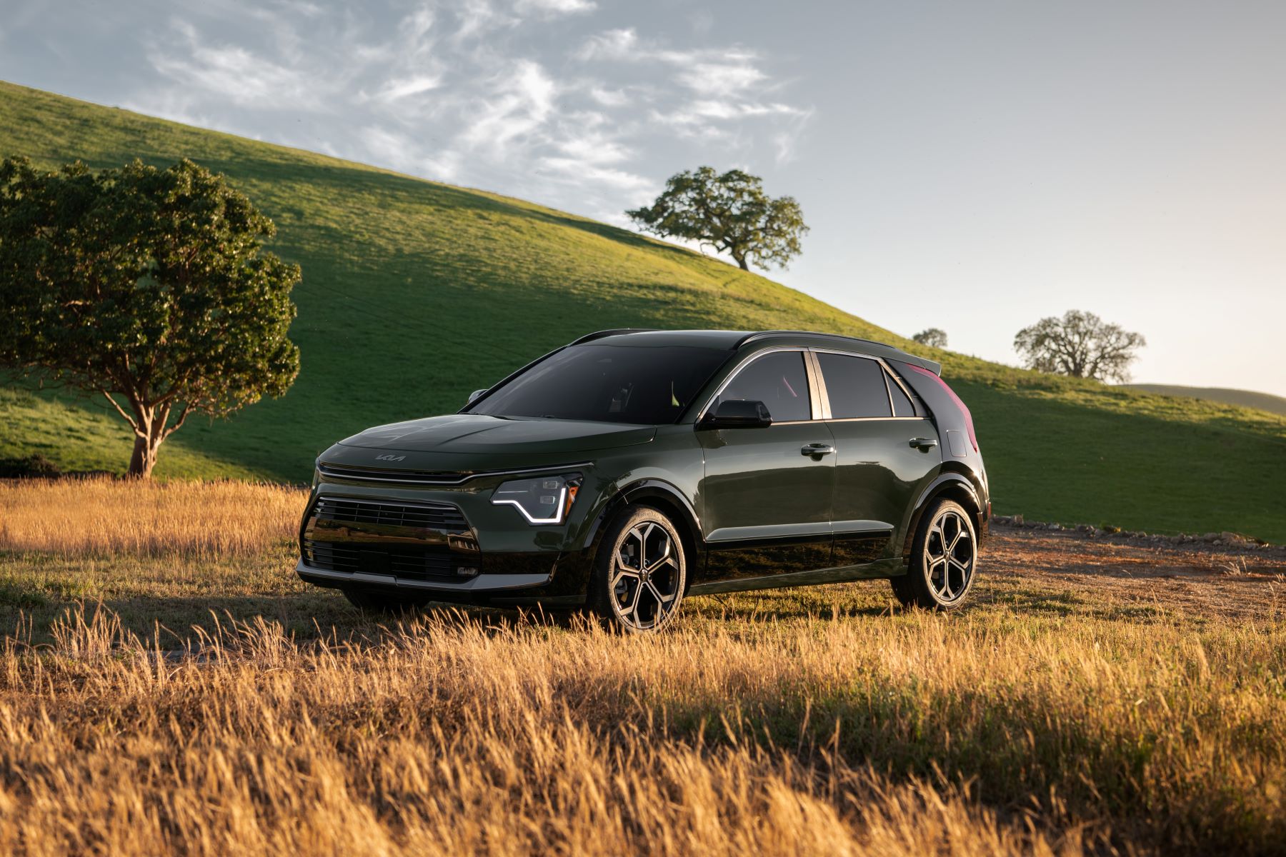 A 2023 Kia Niro hybrid compact SUV model parked near fields of wheat next to grassy hills