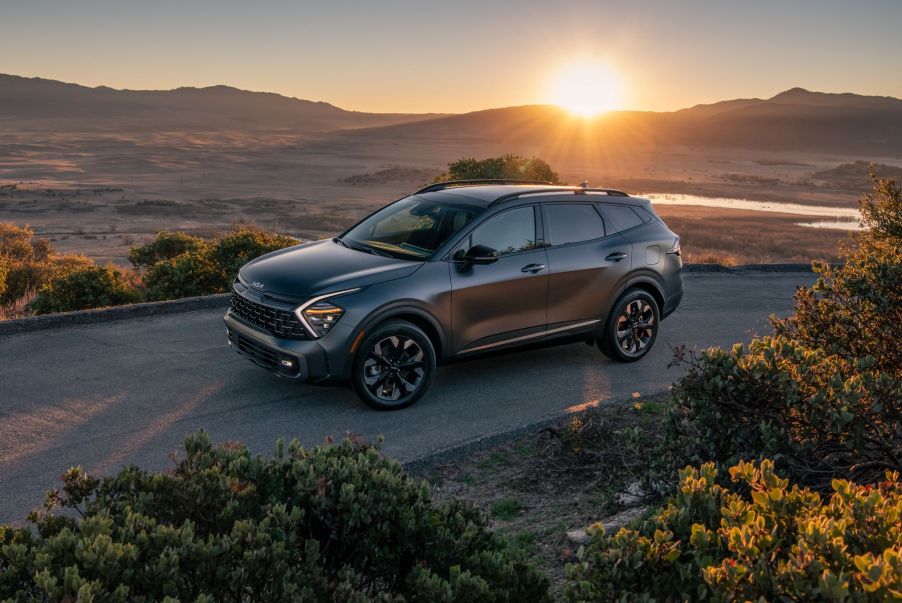 A gray 2023 Kia Sportage plug-in hybrid electric vehicle (PHEV) parked near patches of greenery as the sun sets