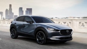 A gray 2023 Mazda CX-30 subcompact SUV is driving on the road.