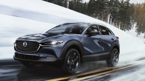 A blue 2023 Mazda CX-30 subcompact SUV is driving on a wet road.