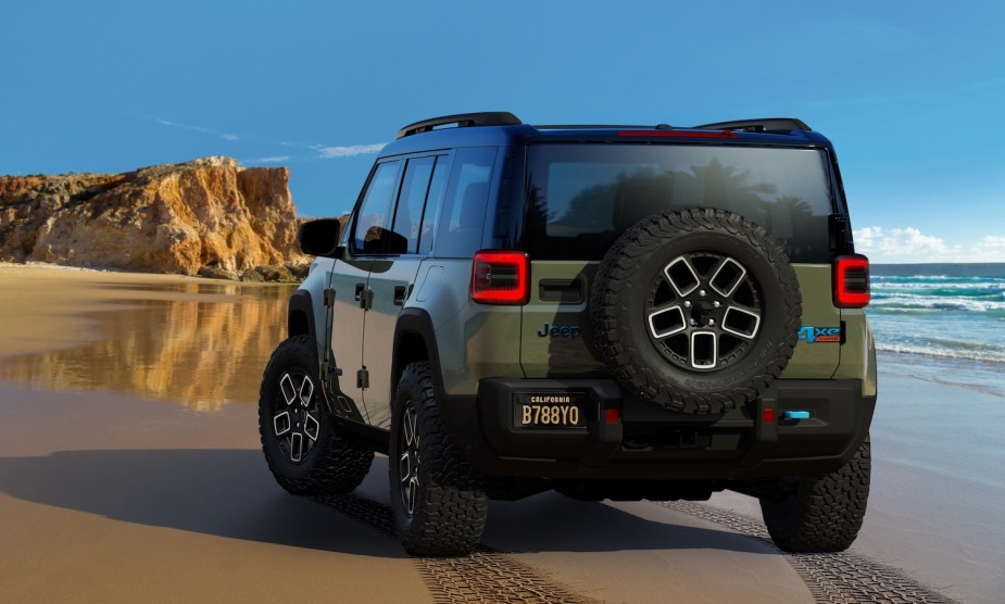 Green Jeep Recon electric SUV parked on a beach, rocks visible in the background.