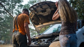 Two people looking under the hood, potentially at the wrong spark plugs.