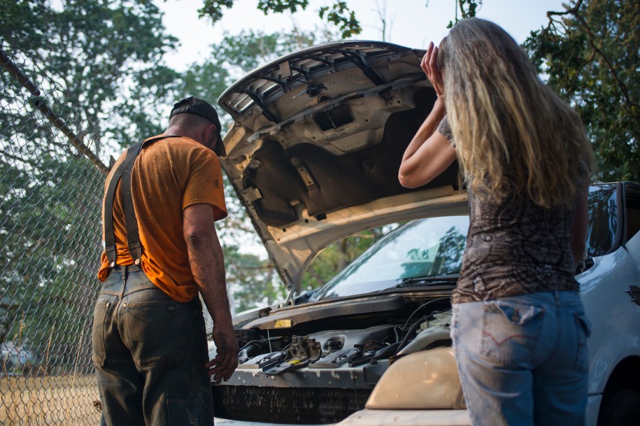 Two people looking under the hood, potentially at the wrong spark plugs. 