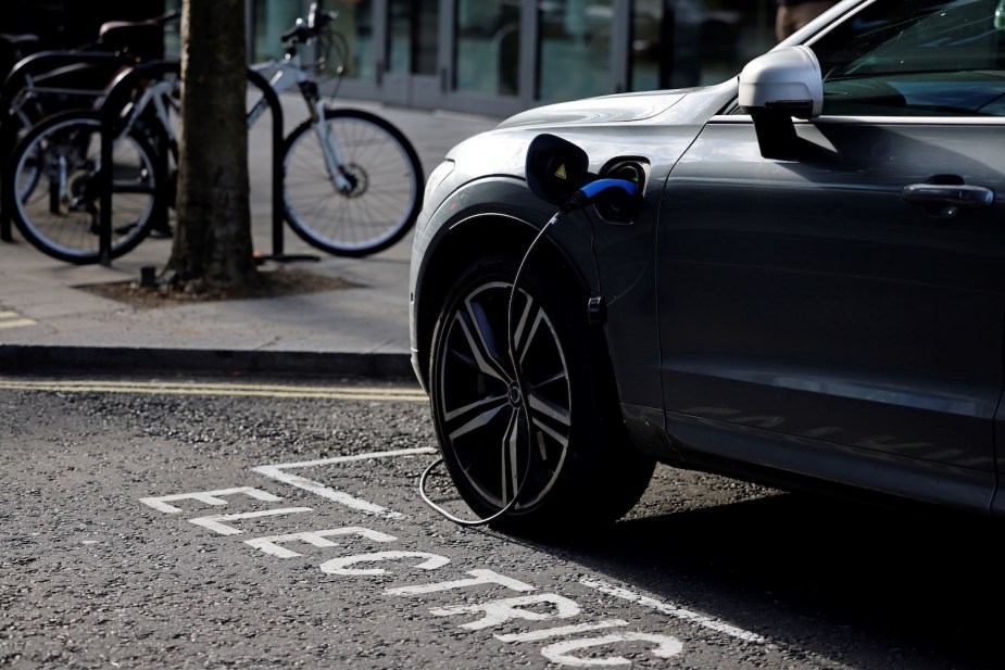 Closeup of a charger attached to an EV on a city street in a parking space labeled "electric."