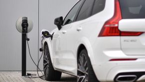 Closeup of a white Volvo plug-in hybrid charging its battery in front of a dealership.