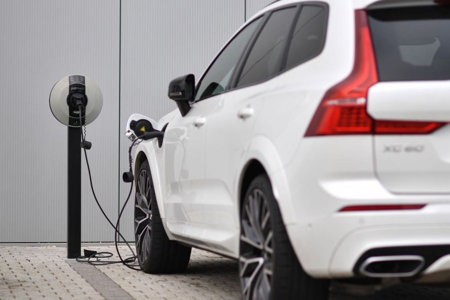 Closeup of a white Volvo plug-in hybrid charging its battery in front of a dealership.