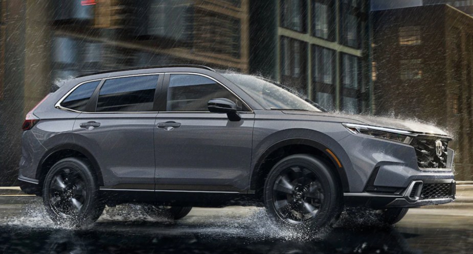 A gray 2023 Honda CR-V small SUV is driving on a damp road. 