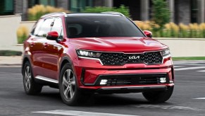 A red 2023 Kia Sorento Hybrid midsize hybrid SUV is driving on the road.