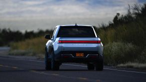 Silver Rivian truck driving away from the camera on a rural highway.