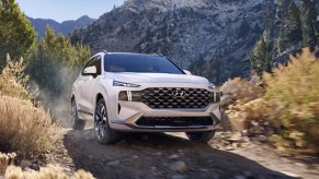 A white 2023 Hyundai Santa Fe midsize SUV is driving off-road.