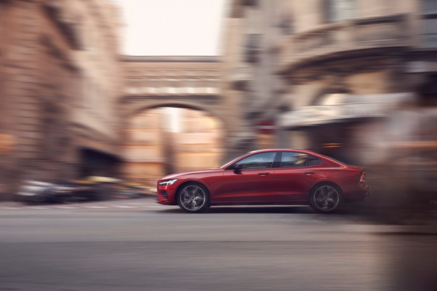 A red Volvo S60 driving on a historic city street.