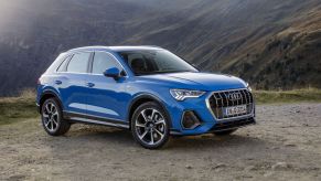 A blue Audi Q3 luxury subcompact SUV model parked on a plain of drip near mountains