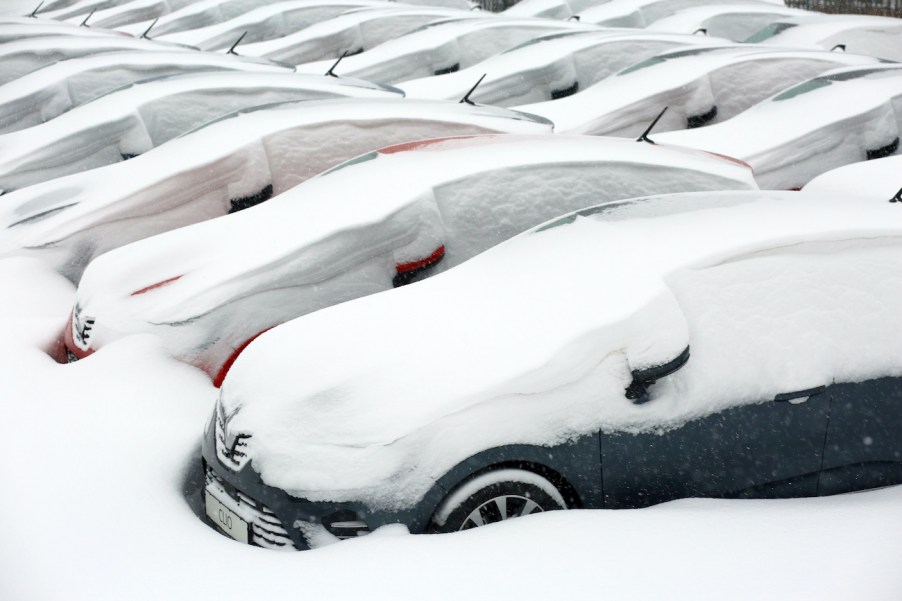 Vehicles are covered in snow in the yard of a car dealership.