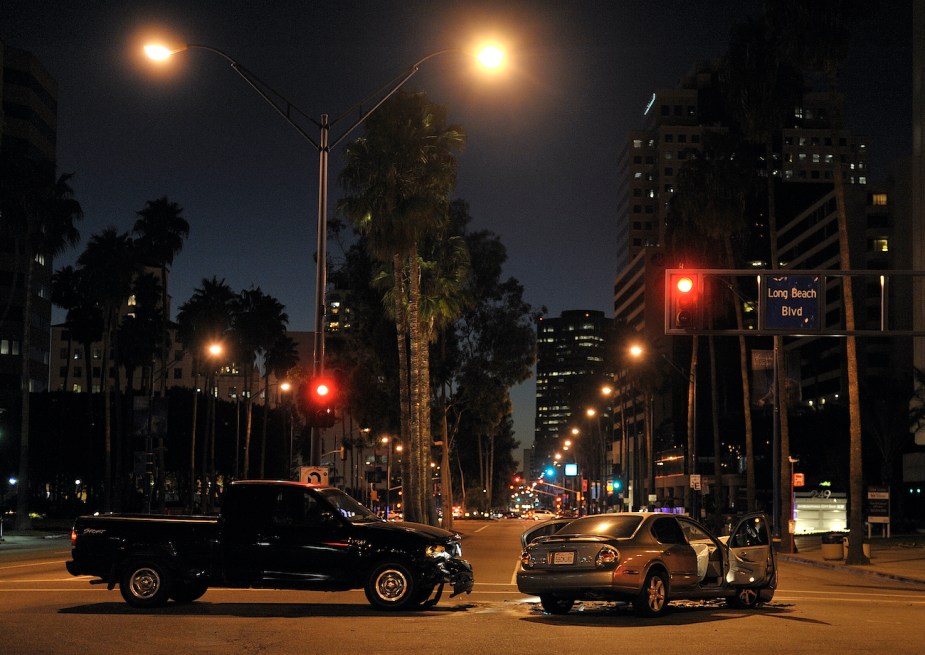 A beige car driven and pickup truck sit at an intersection after colliding during rush hour traffic.