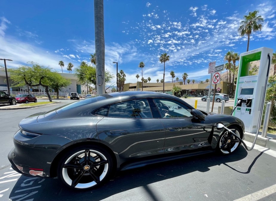 A Porsche Taycan sports car parked in a parking lot, a charging cable attached to its fender.