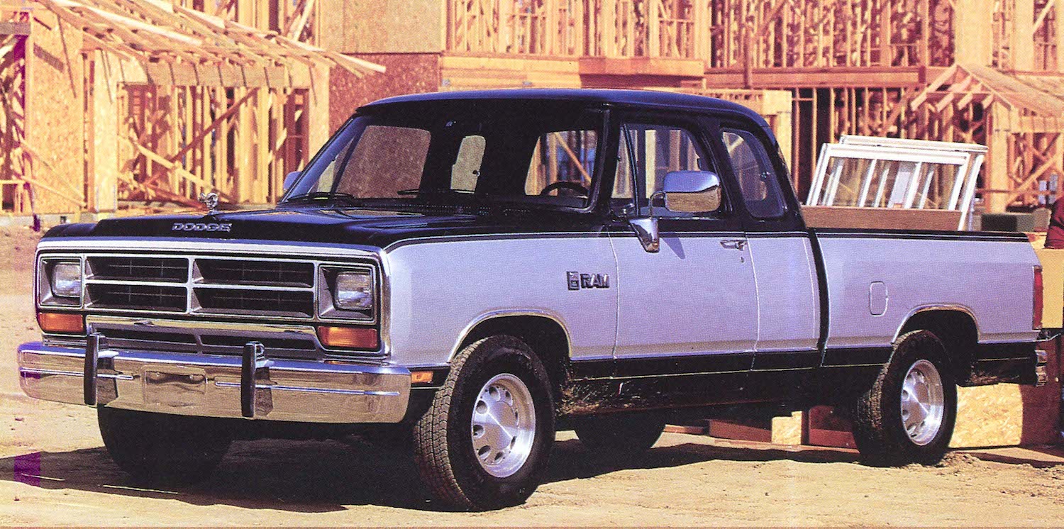 A 1990 Dodge Ram D150 pickup truck with two-tone paint, parked in front of a construction site.