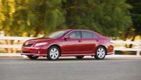 A red 2009 Toyota Camry driving alongside a fence