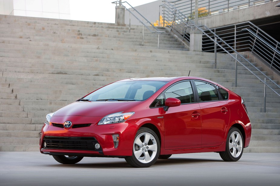 A red 2012 Toyota Prius hybrid compact sedan parked in front of the concrete stairway of a modern building.