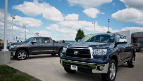 Two full-size Toyota Tundra pickup trucks parked in front of a Toyota dealership, a blue sky visible in the background.