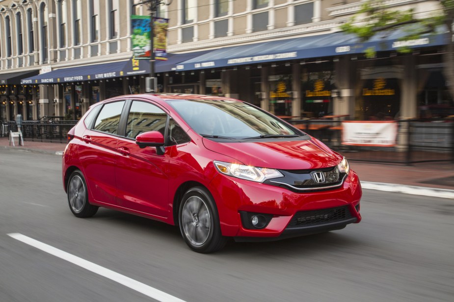 A red 2016 Honda Fit driving down a city street