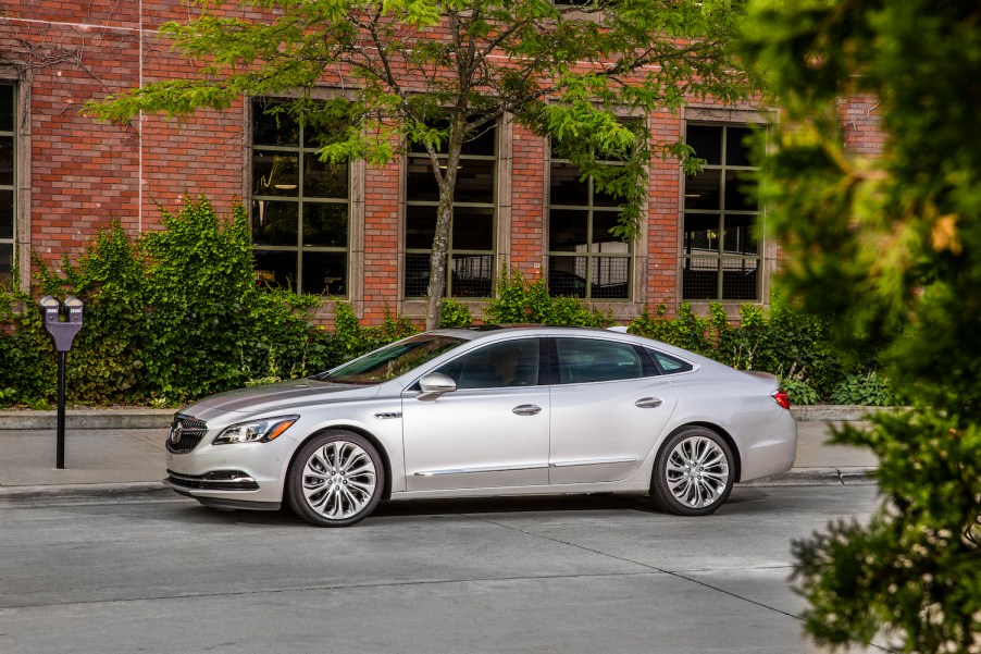 Silver Buick LaCrosse sedan parked in front of a brick wall, leaves visible in the foreground.