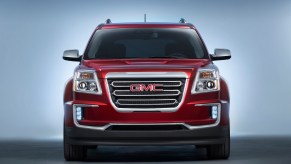 Publicity photo of the large, chrome grille of a red GMC Terrain crossover SUV parked in a studio, a white background behind it.