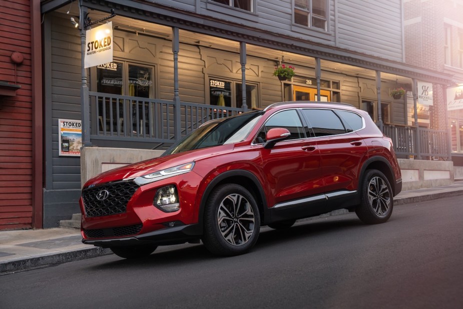 A red Hyundai Santa Fe parked in front of a gray storefront, a balcony railing visible in the background.