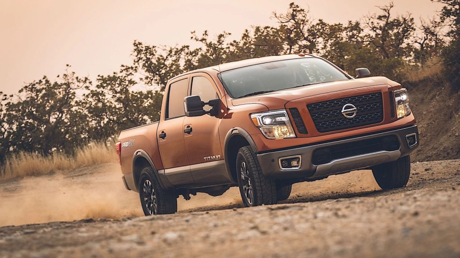 Orange 2019 Nissan Titan full-size pickup truck driving along a dirt road.