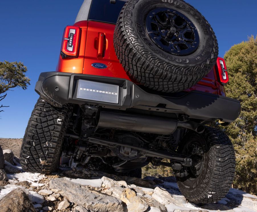 An orange 2022 Ford Bronco Wildtrak off-road SUV model with option HOSS 3.0 climbing over a hill of rocks