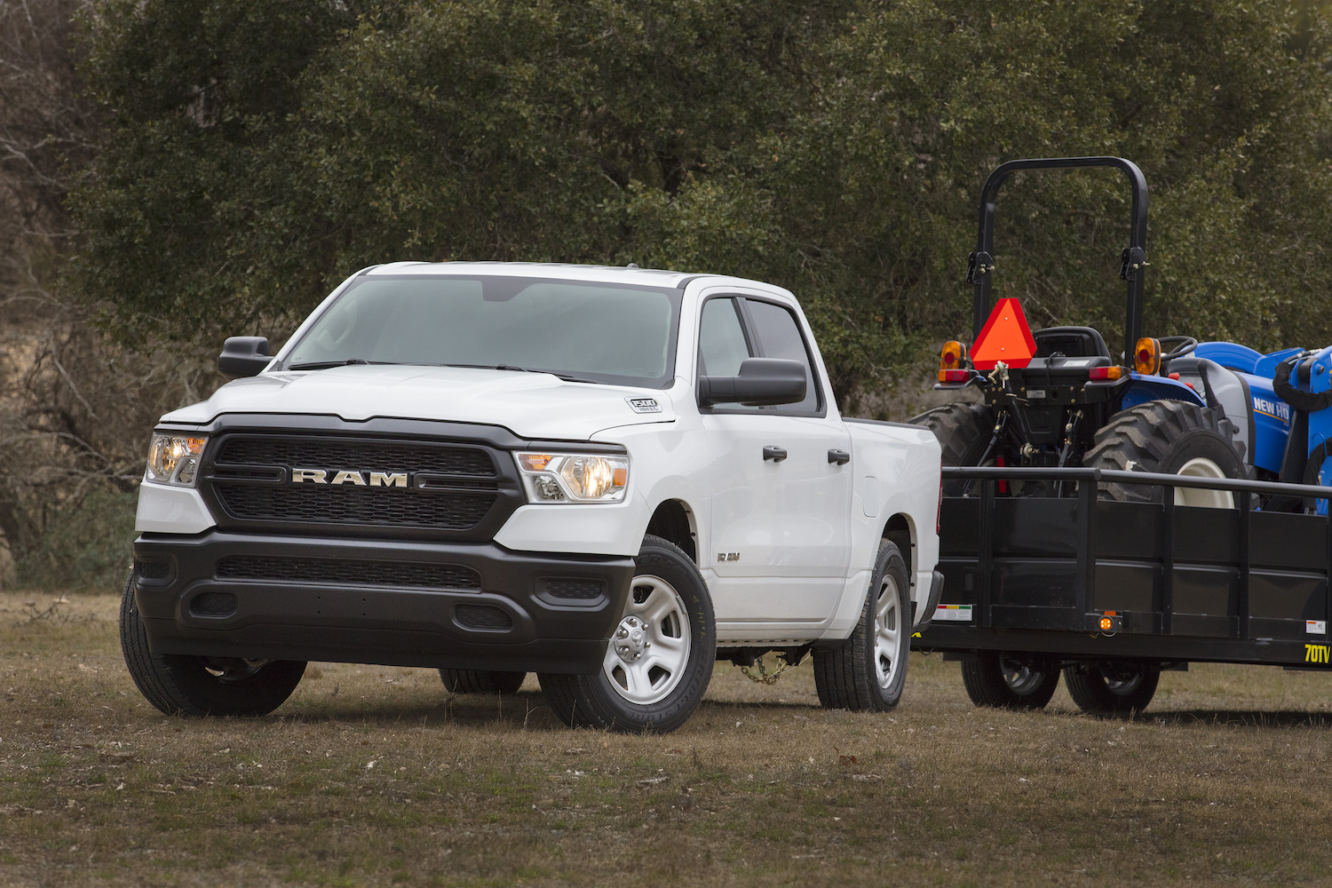 A white Ram 1500 tradesman work truck hooked up to a trailer with a tractor on top of it.