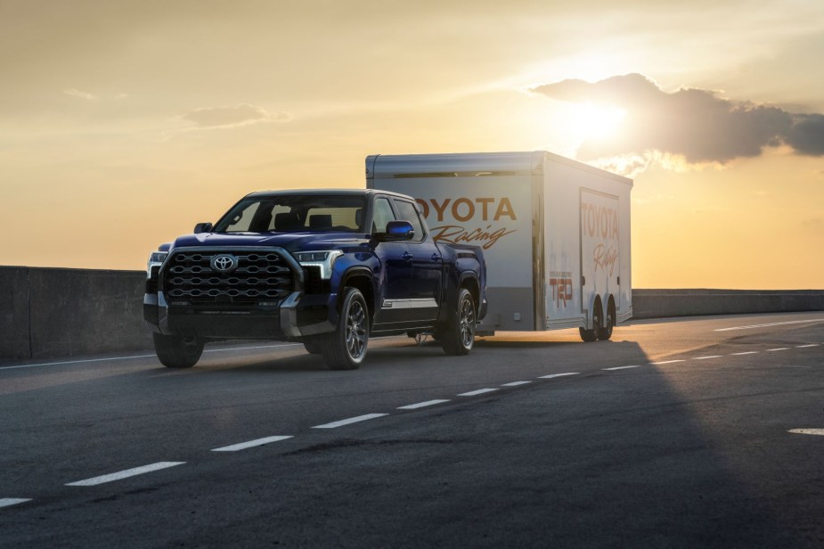 A dark blue 2022 Toyota Tundra full-size pickup truck towing a Toyota Racing trailer on a highway at sunset