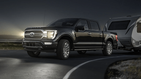 A black 2023 Ford F-150 full-size pickup truck with LED fog lamps towing a camper at night