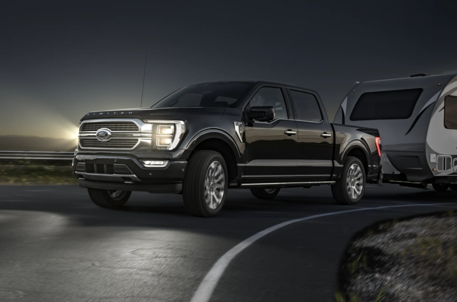 A black 2023 Ford F-150 full-size pickup truck with LED fog lamps towing a camper at night