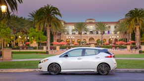 A white 2023 Nissan Leaf in front of a building in a tropical area.