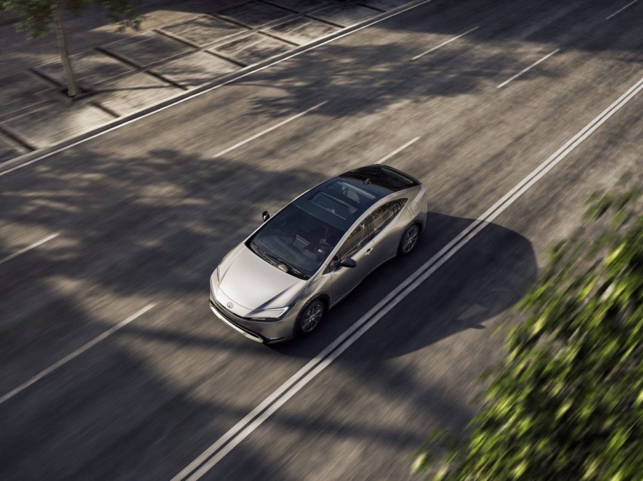 A white 2023 Toyota Prius driving down the road from an aerial view.