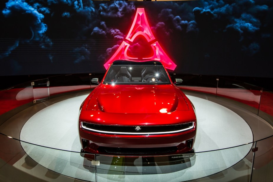 Red Dodge Charger SRT Banshee concept EV on stage at an auto show, an advertisement playing in the background.