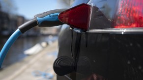 A blue aftermarket EV charging cable plugged into a Tesla's port, the electric car's black fender and tail light visible in the foreground.