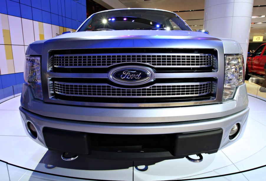 The grille of a silver Ford F-150 pickup truck parked on the stage at an auto show.