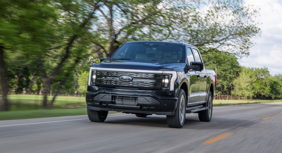 A black Ford F-150 Lightning Platinum all-electric pickup truck model driving on a country highway