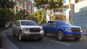 Two Ford Maverick small pickup trucks driving side by side on the road (L) gray, (R) blue.