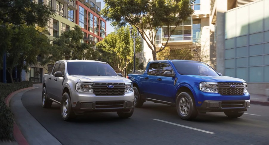 Two Ford Maverick small pickup trucks driving side by side on the road (L) gray, (R) blue.