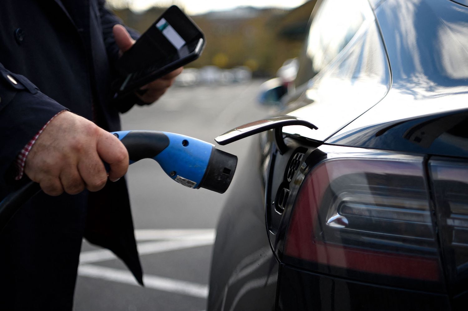 A Tesla owner plugs a free EV charge cable into the port of their EV sedan.