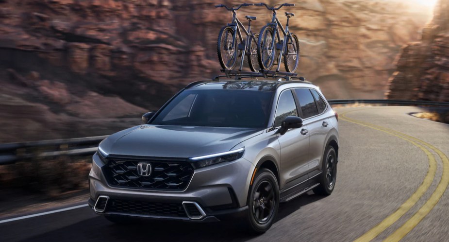 A gray 2023 Honda CR-V Hybrid small SUV is driving on the road. 